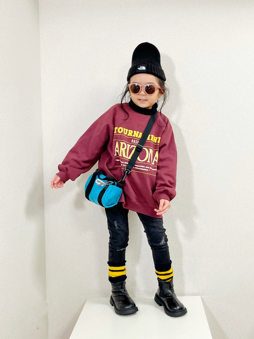 レッド系のスウェット、ブラック系のニット/セーター、ブルー系のショルダーバッグを着用したキッズの冬コーディネートの1枚目の写真