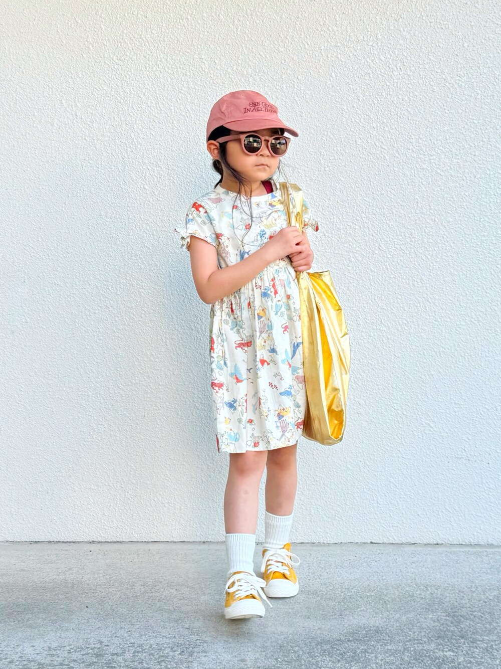 ベージュ系のワンピース、イエロー系のスニーカー、ゴールド系のハンドバッグを着用したキッズの夏コーディネートの1枚目の写真
