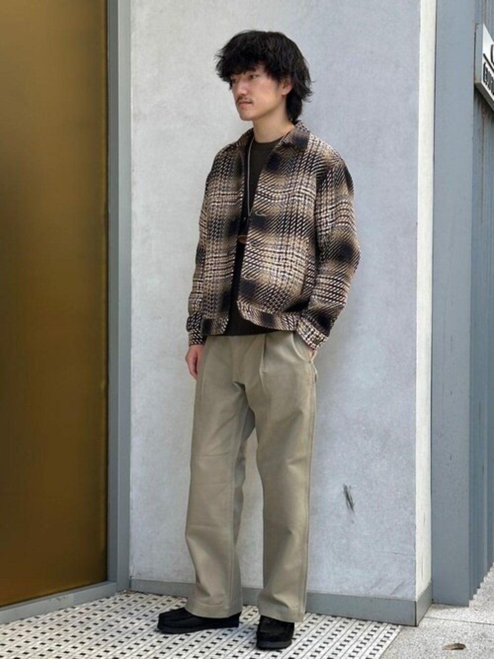 ブラック系のブルゾン、ブラウン系のニット/セーター、ベージュ系のチノパンツを着用したメンズの秋コーディネートの1枚目の写真