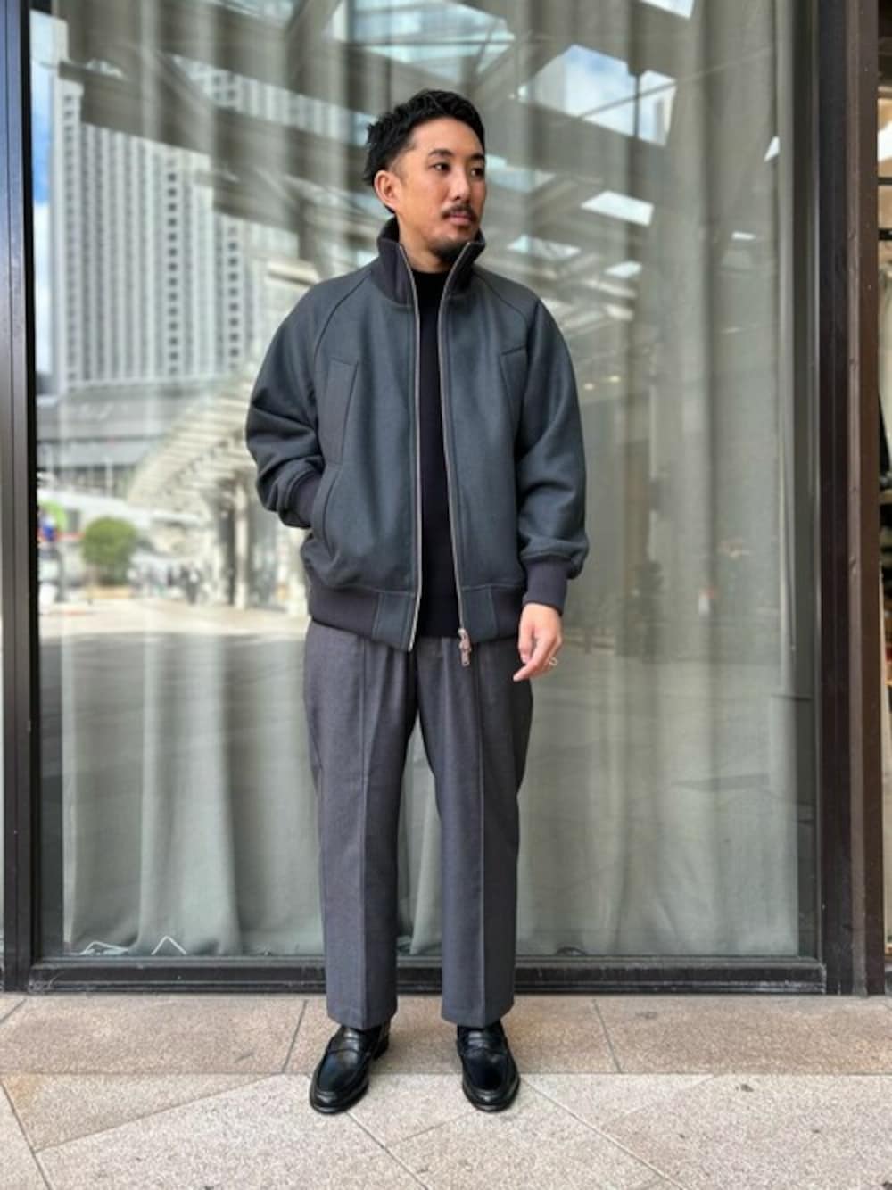 グレー系のブルゾン、ブラック系のニット/セーター、グレー系のスラックスを着用したメンズの秋コーディネートの1枚目の写真