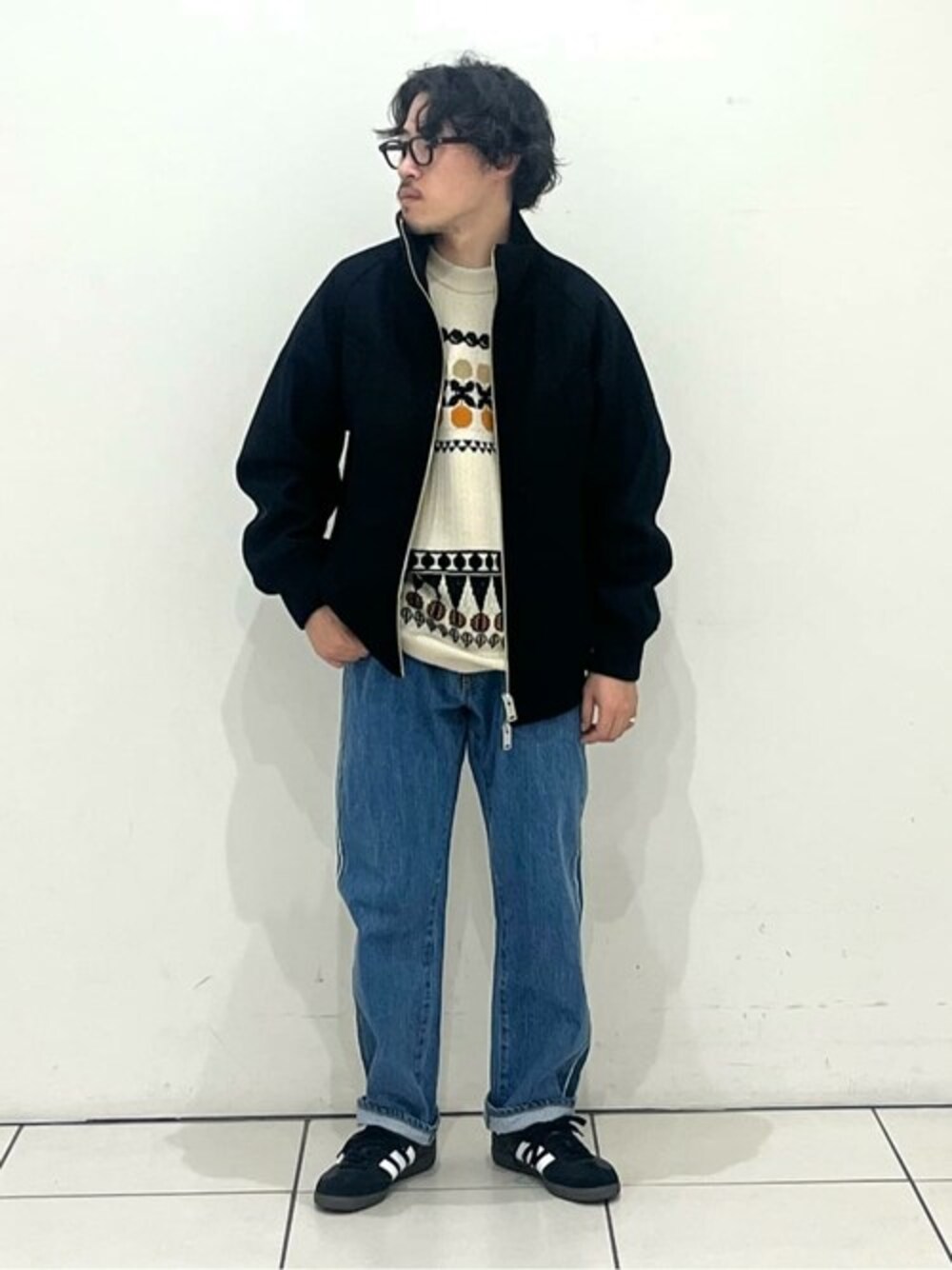 ブラック系のブルゾン、ベージュ系のニット/セーター、ブルー系のデニムパンツを着用したメンズの秋コーディネートの1枚目の写真