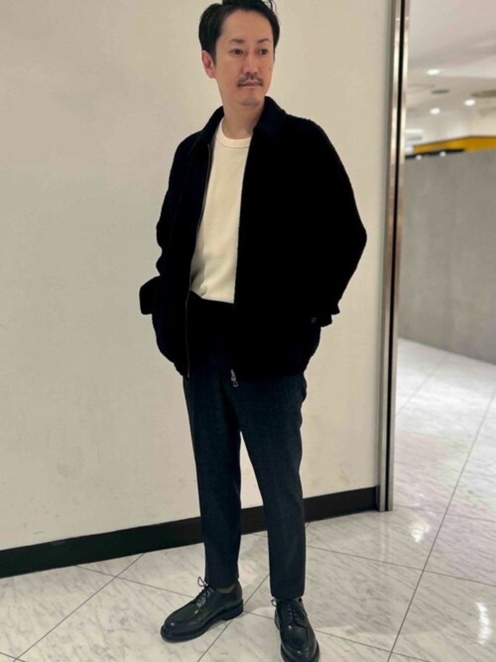 ブラック系のブルゾン、ホワイト系のTシャツ/カットソー、グレー系のスラックスを着用したメンズの秋コーディネートの1枚目の写真