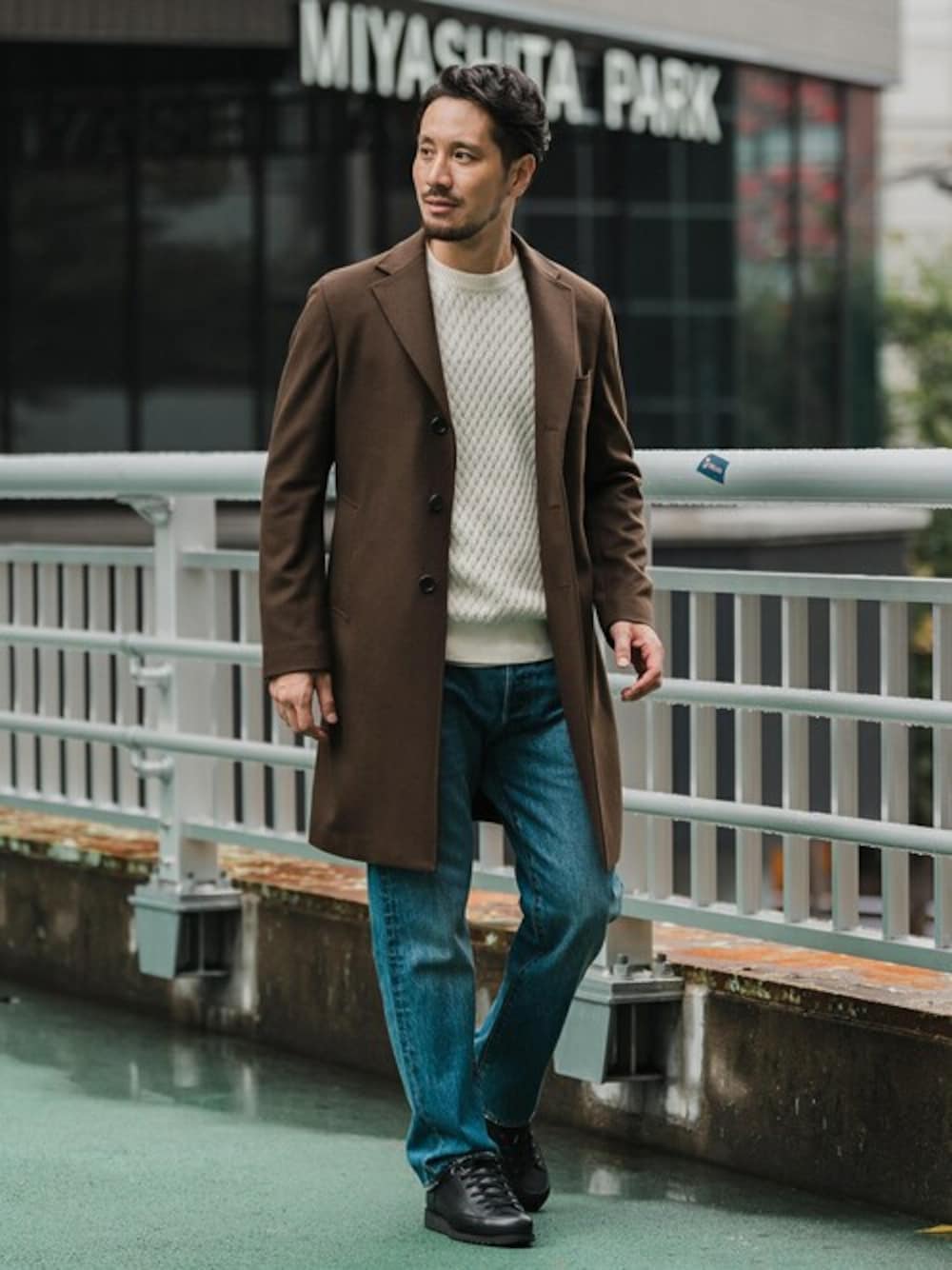 ブラウン系のチェスターコート、ホワイト系のニット/セーター、ブルー系のデニムパンツを着用したメンズの冬コーディネートの1枚目の写真