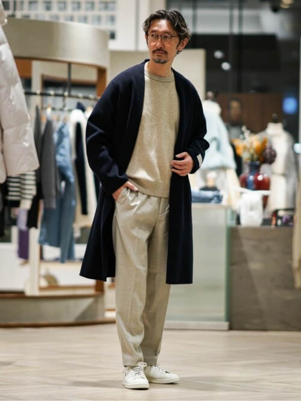 ブルー系のノーカラーコート、ベージュ系のニット/セーター、ベージュ系のスラックスを着用したメンズの冬コーディネートの1枚目の写真