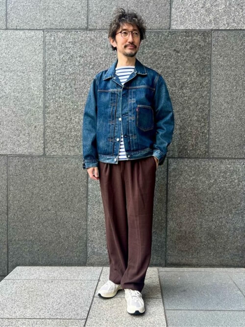 ブルー系のデニムジャケット、ブラウン系のスラックス、グレー系のスニーカーを着用したメンズの冬コーディネートの1枚目の写真
