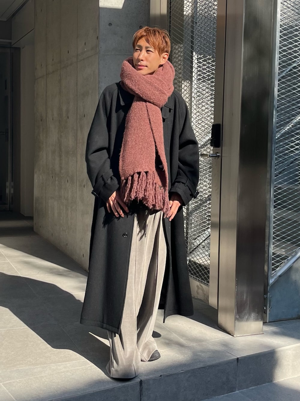 グレー系のその他パンツ、ブラック系のステンカラーコート、レッド系のマフラーを着用したメンズの秋コーディネートの1枚目の写真