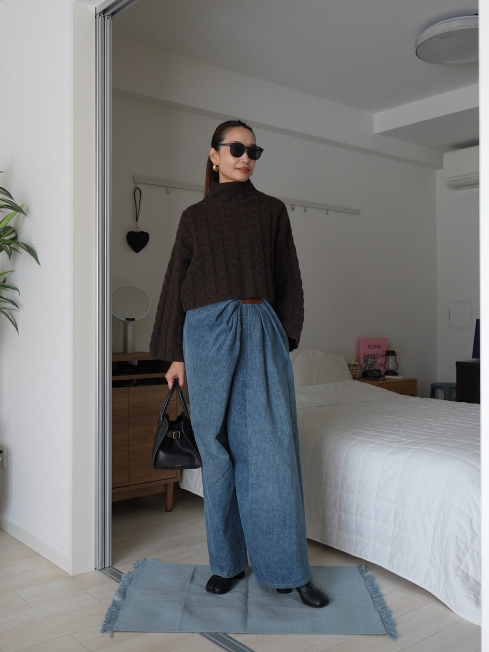 ブラウン系のニット/セーター、ブルー系のデニムパンツ、ブラック系のバッグを着用したレディースの秋コーディネートの1枚目の写真