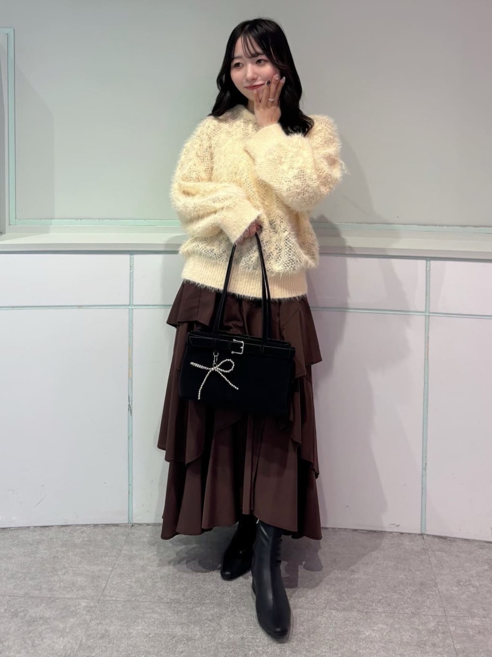 イエロー系のニット/セーター、ブラウン系のスカート、ブラック系のブーツを着用したレディースの秋コーディネートの1枚目の写真