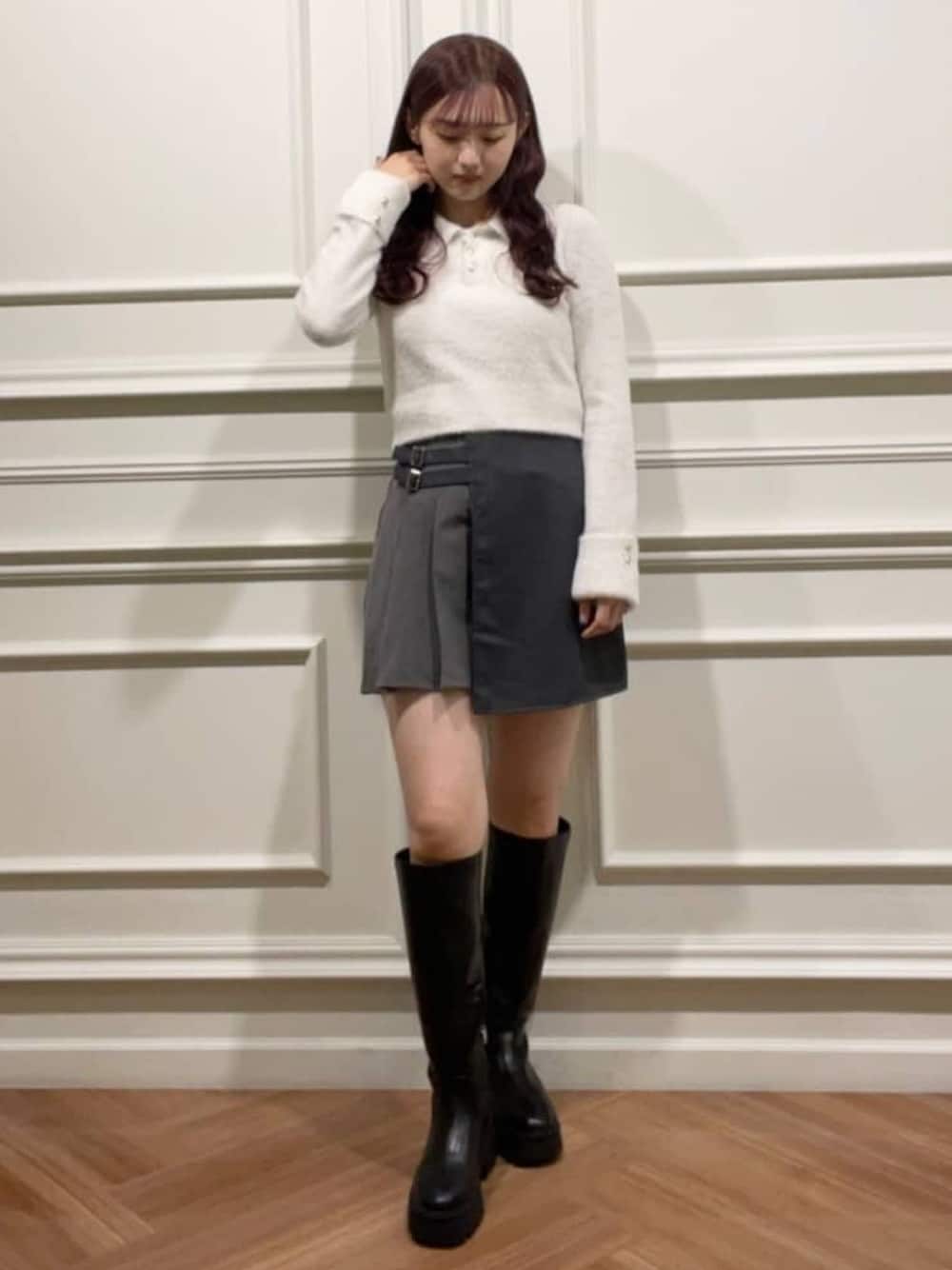 グレー系のスカート、ホワイト系のニット/セーター、ブラック系のブーツを着用したレディースの冬コーディネートの1枚目の写真