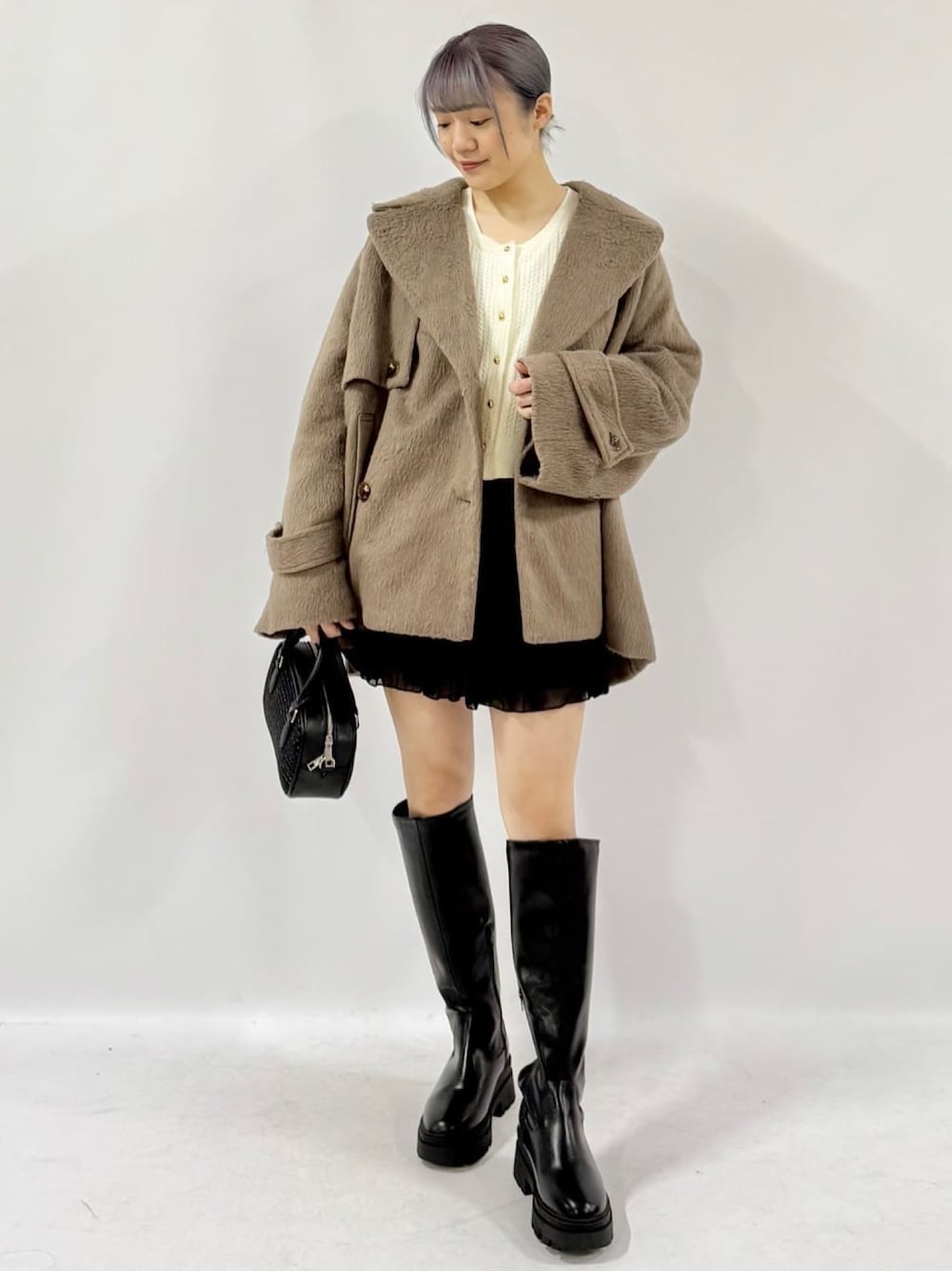 ブラック系のチェスターコート、ブラック系のスカート、ホワイト系のカーディガン/ボレロを着用したレディースの冬コーディネートの1枚目の写真