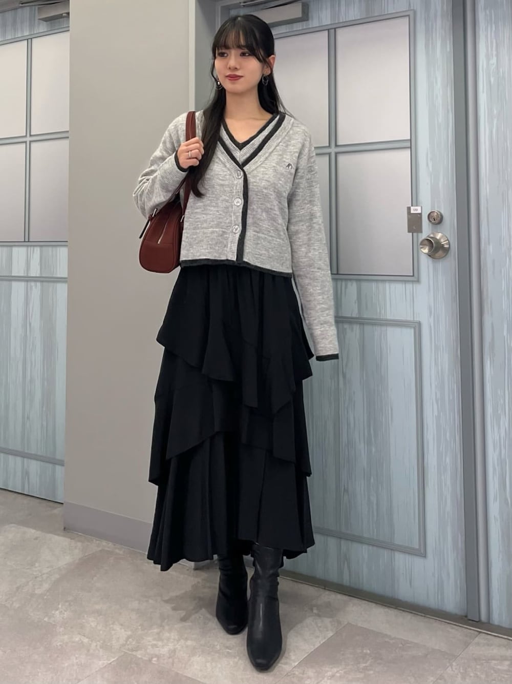 グレー系のアンサンブル、ブラック系のスカートを着用したレディースの秋コーディネートの1枚目の写真