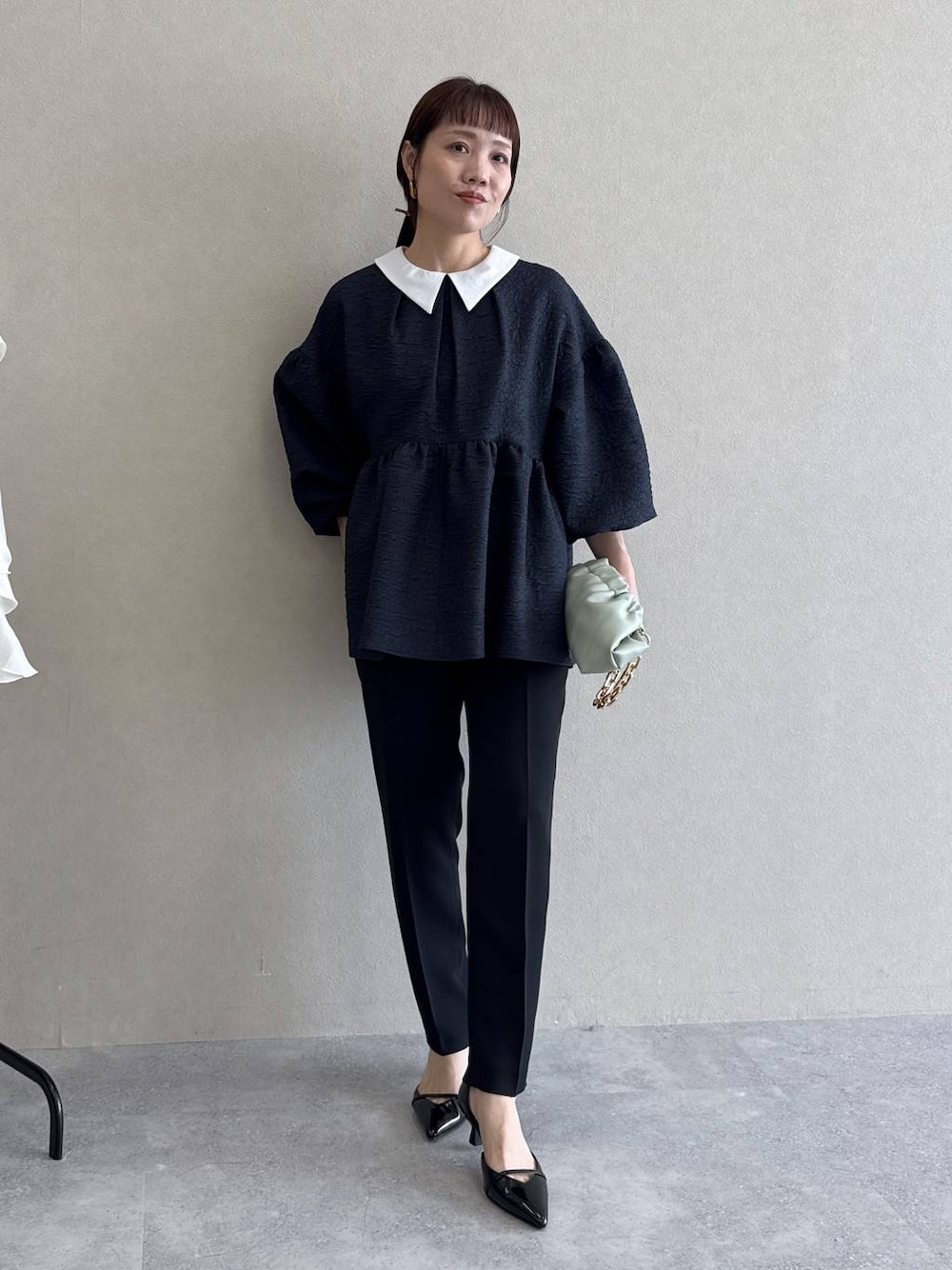 ブラック系のパンプス、グリーン系のショルダーバッグ、ブルー系のパンツドレスを着用したレディースの冬コーディネートの1枚目の写真