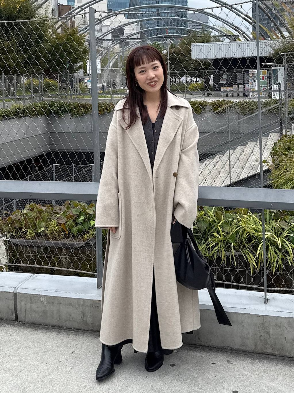 ベージュ系のステンカラーコート、ブラック系のブーツ、グレー系のカーディガン/ボレロを着用したレディースの秋コーディネートの1枚目の写真