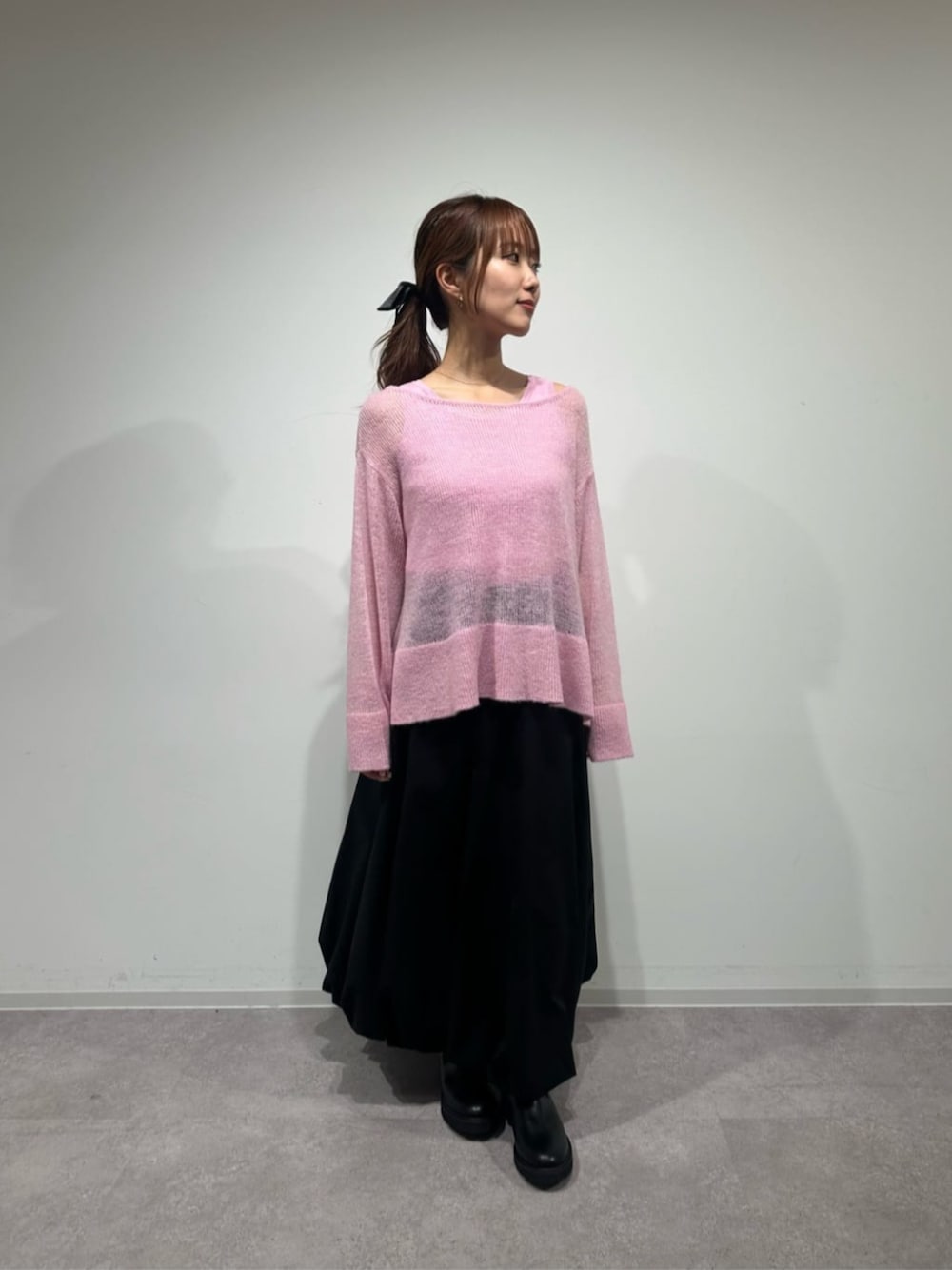 ピンク系のニット/セーター、ブラック系のスカート、ブラック系のブーツを着用したレディースの秋コーディネートの1枚目の写真