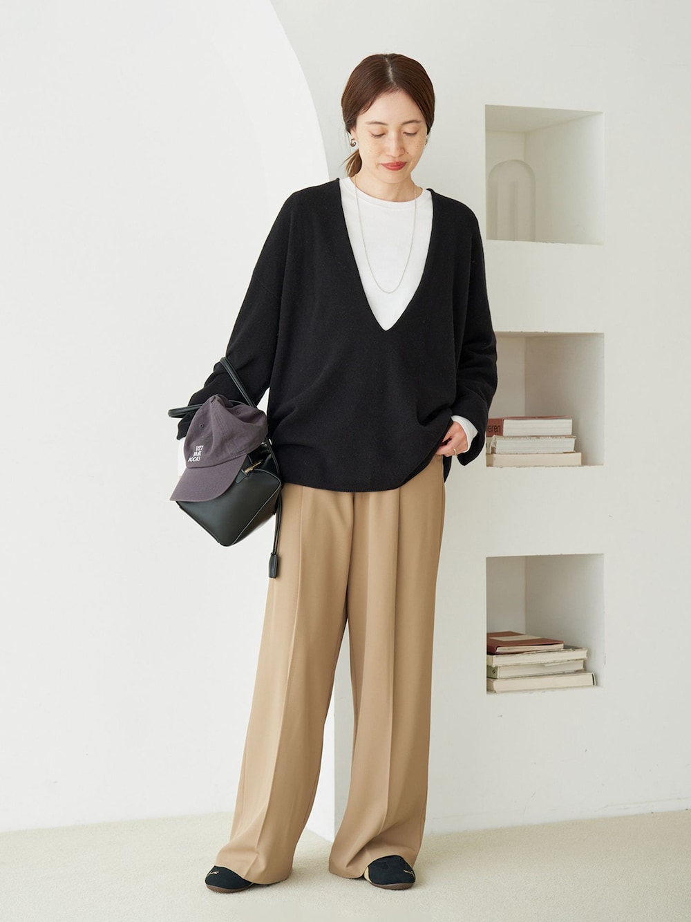 ベージュ系のスラックス、グレー系のTシャツ/カットソー、ブラック系のニット/セーターを着用したレディースの秋コーディネートの1枚目の写真