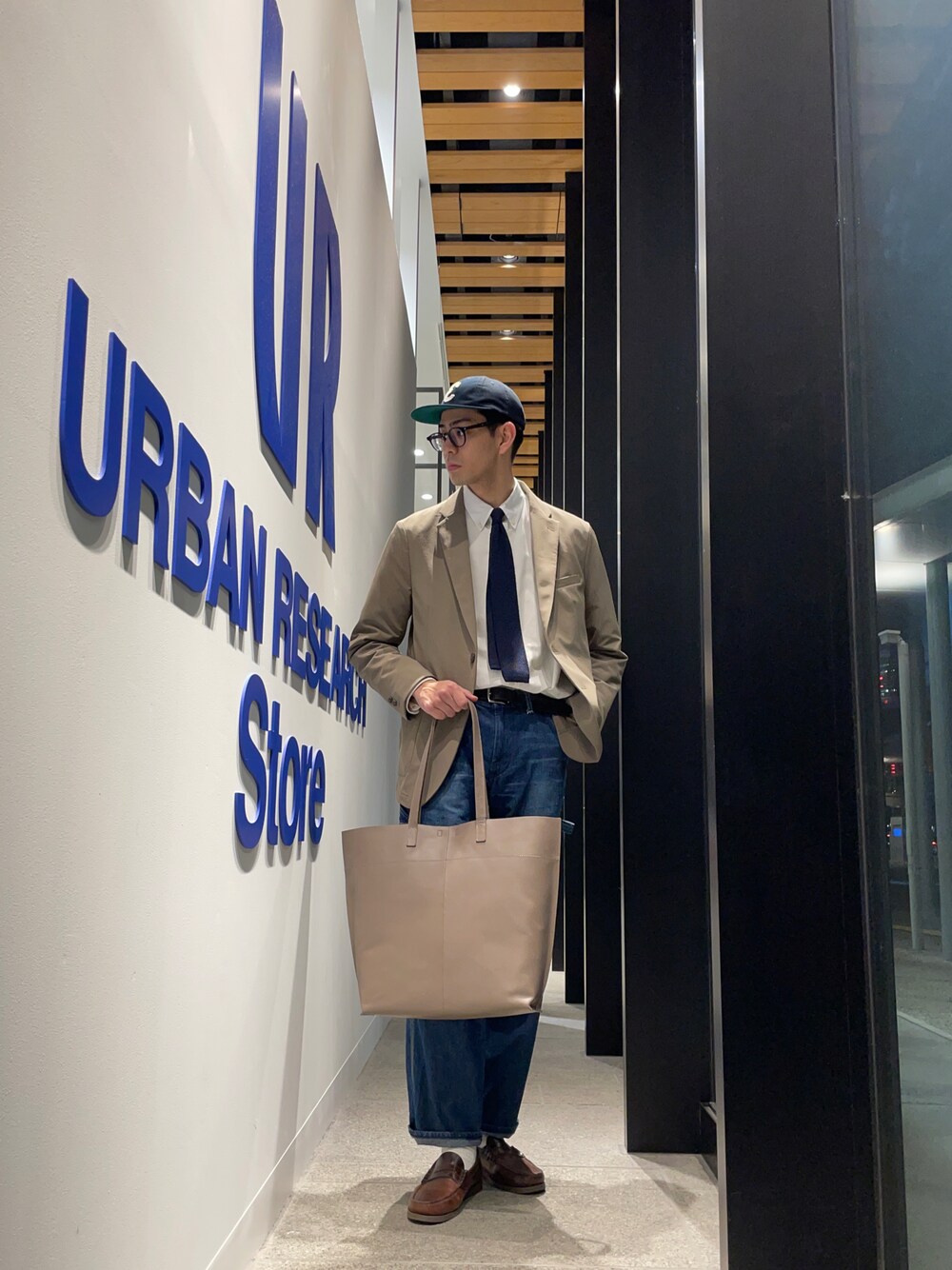 ブラウン系のスーツジャケット、ブルー系のネクタイ、グレー系のトートバッグを着用したメンズの春コーディネートの1枚目の写真