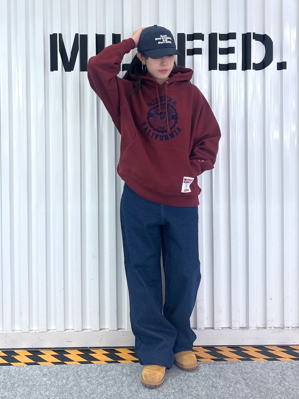 レッド系のパーカー、ブルー系のデニムパンツ、ブルー系のキャップを着用したレディースの秋コーディネートの1枚目の写真