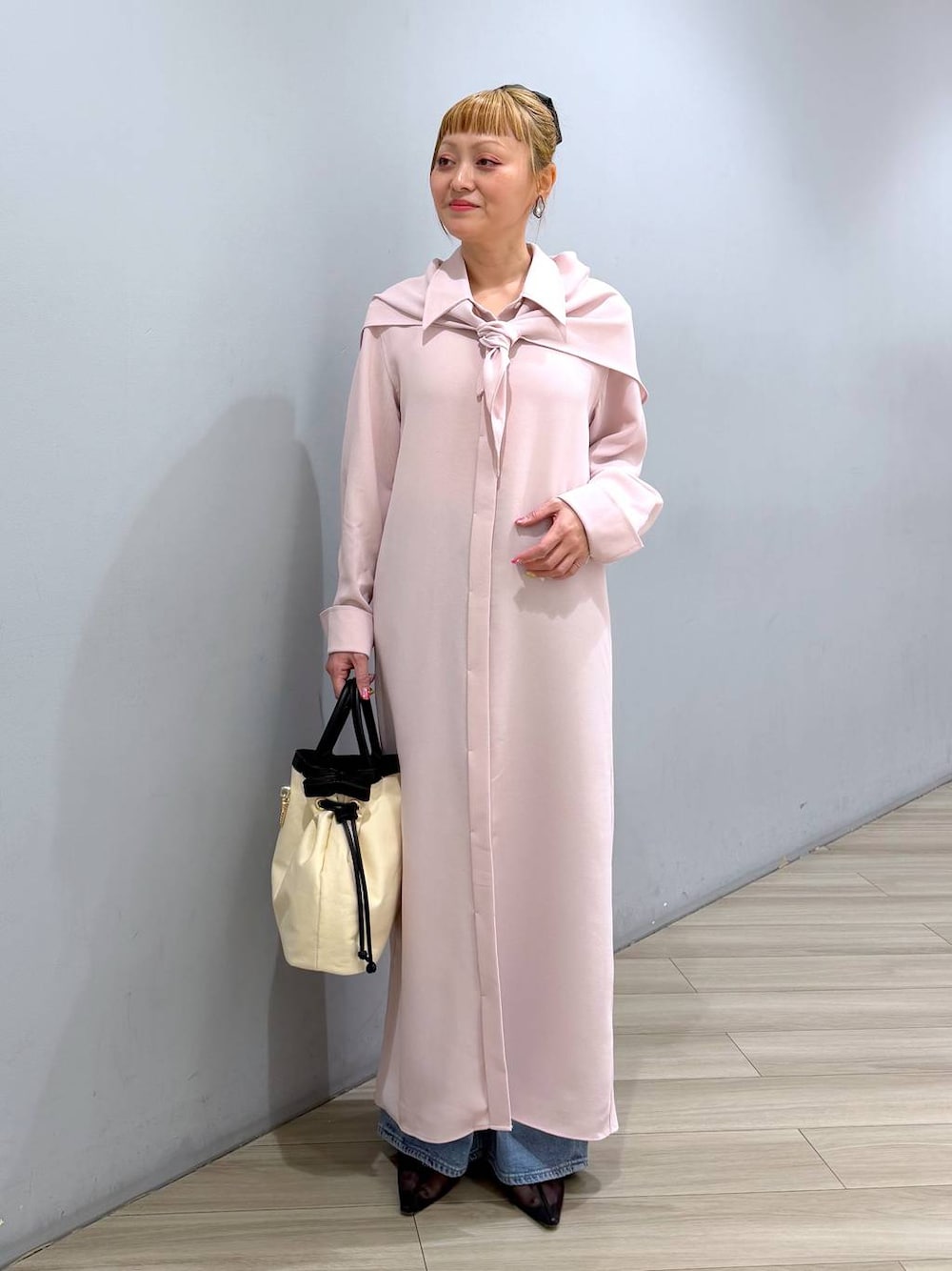 ピンク系のシャツワンピース、ブルー系のデニムパンツ、ホワイト系のハンドバッグを着用したレディースの冬コーディネートの1枚目の写真