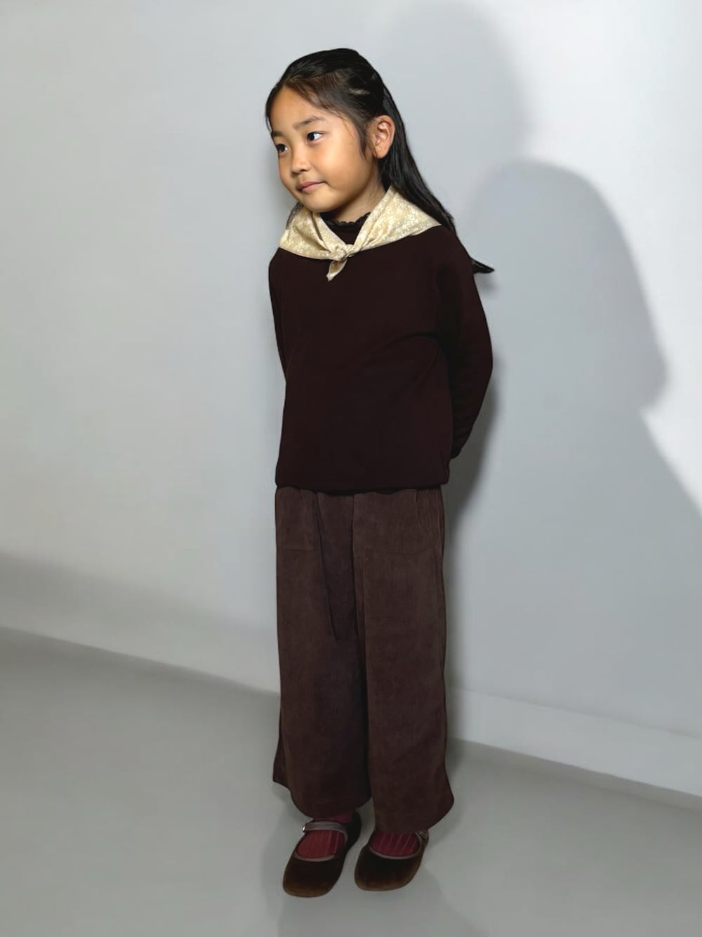 ブラウン系のトップス、ブラウン系のパンツ、ベージュ系のストール/ショールを着用したキッズの秋コーディネートの1枚目の写真
