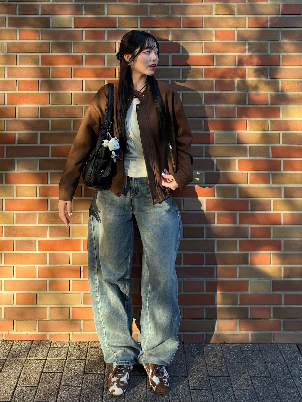 ブラウン系のスニーカー、ブラウン系のライダースジャケット、ブルー系のデニムパンツを着用したレディースの秋コーディネートの1枚目の写真