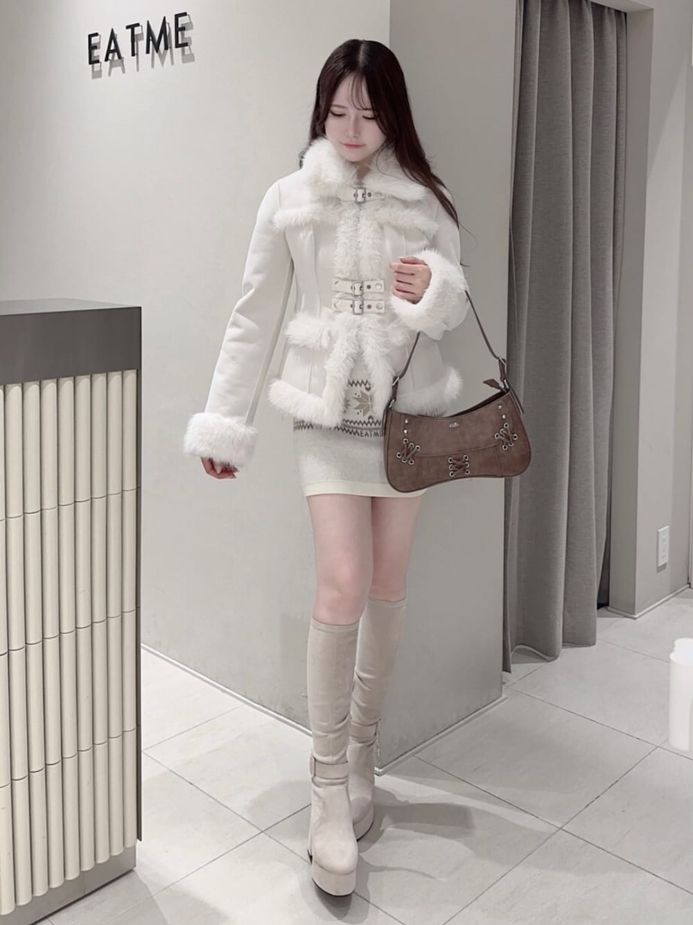 ブラウン系のショルダーバッグ、ホワイト系のブーツ、ホワイト系のスカートを着用したレディースの秋コーディネートの1枚目の写真