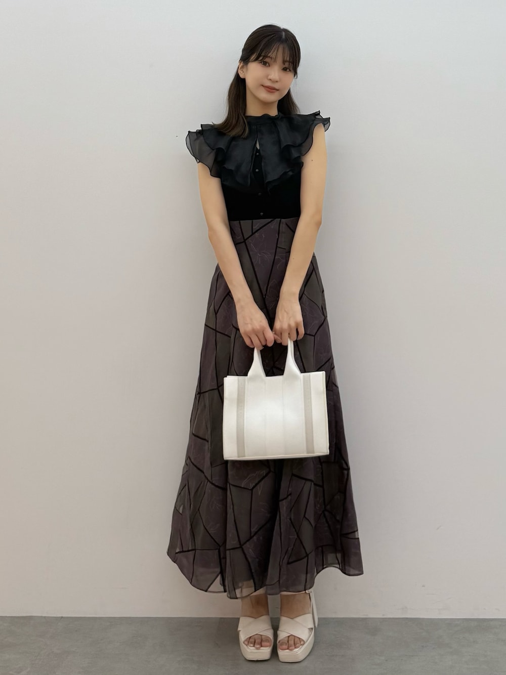 ブラック系のニット/セーター、ブラウン系のスカート、ホワイト系のトートバッグを着用したレディースの夏コーディネートの1枚目の写真