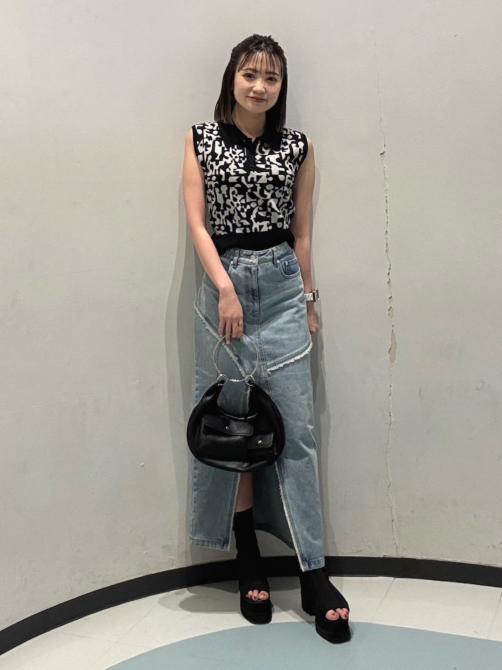 ブラック系のニット/セーター、ブルー系のデニムスカート、ブラック系のサンダルを着用したレディースの夏コーディネートの1枚目の写真