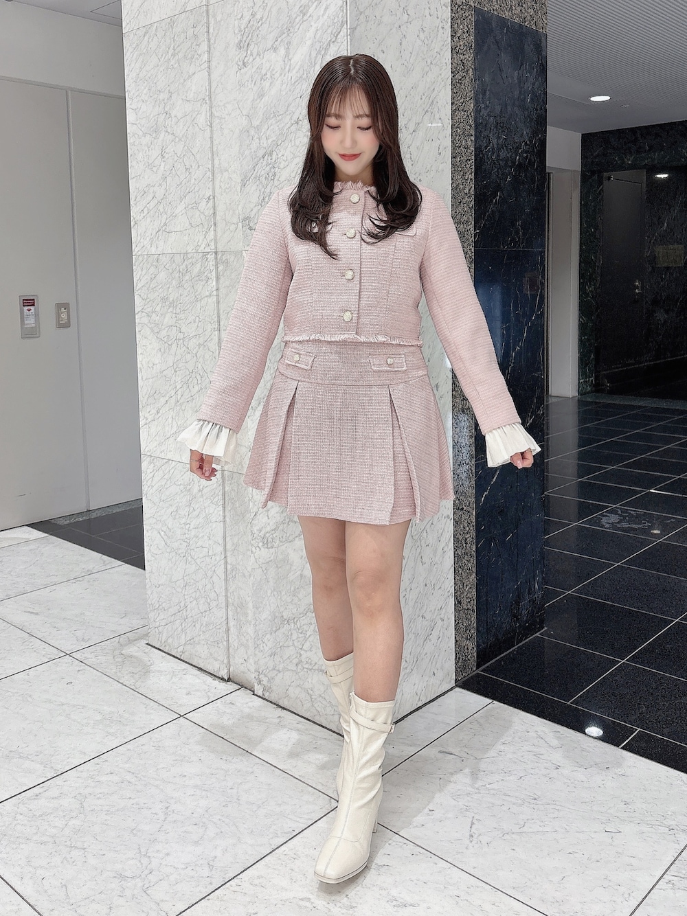 ピンク系のノーカラージャケット、ピンク系のスカート、ホワイト系のブーツを着用したレディースの冬コーディネートの1枚目の写真