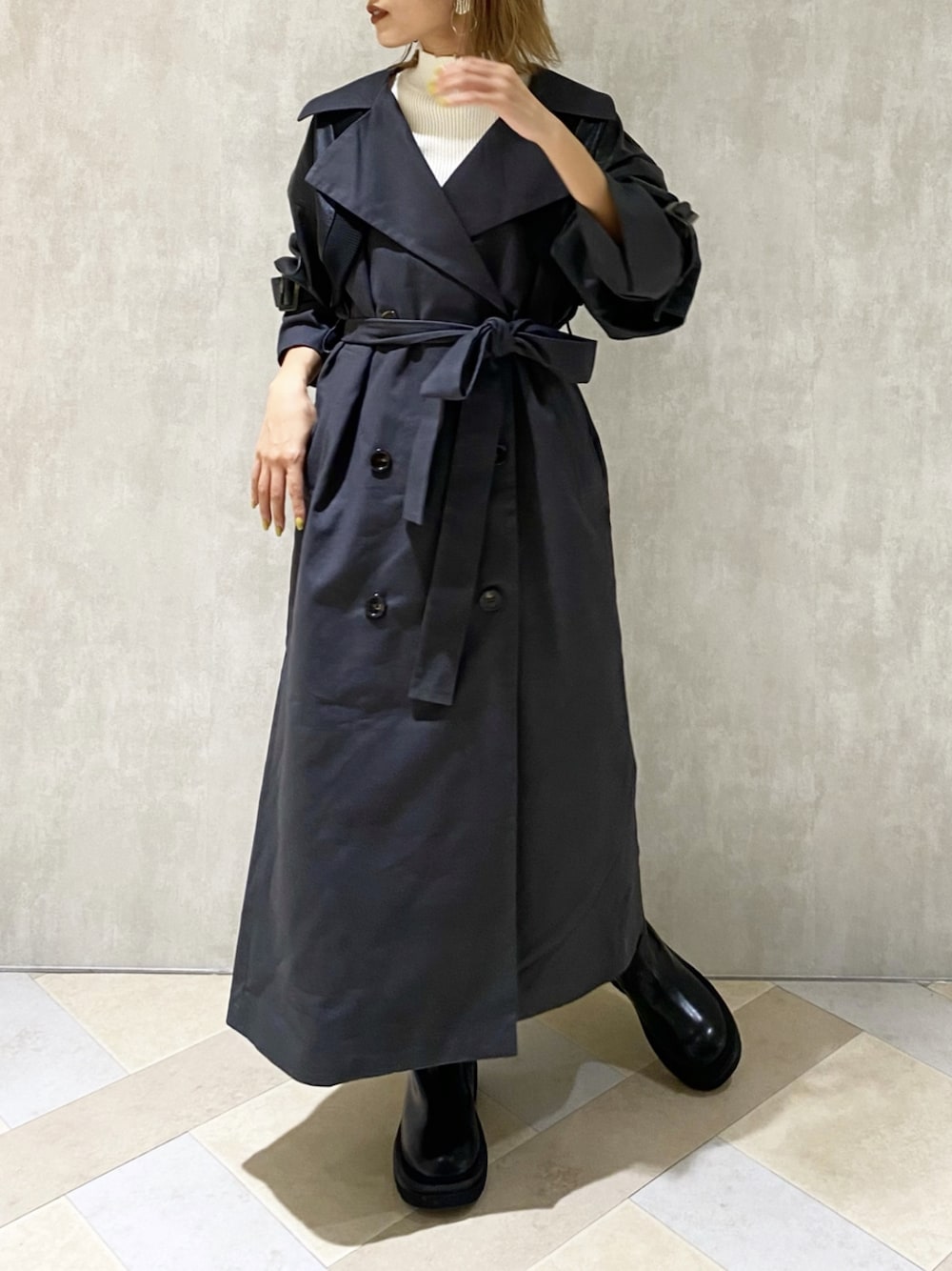 ホワイト系のニット/セーター、グレー系のトレンチコート、ブラック系のブーツを着用したレディースの秋コーディネートの1枚目の写真