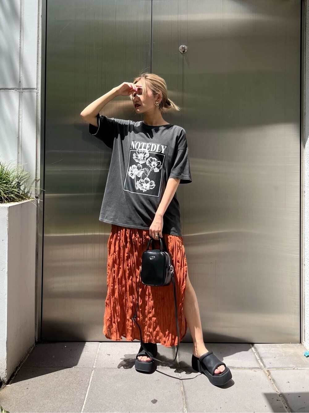 ブラック系のショルダーバッグ、オレンジ系のワンピース、ブラック系のサンダルを着用したレディースの春コーディネートの1枚目の写真