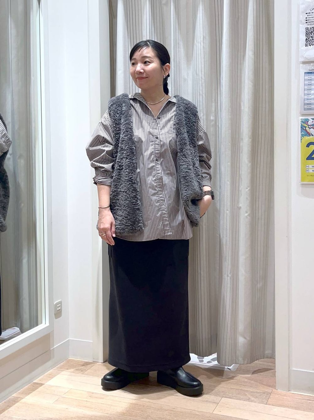 グレー系のベスト、ブラック系のスカート、ブラック系のブーツを着用したレディースの秋コーディネートの1枚目の写真