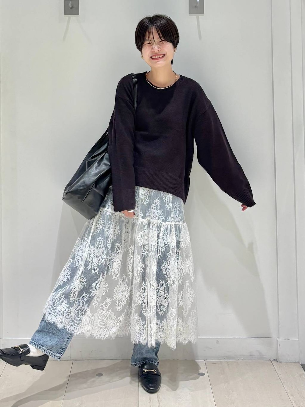 ブラック系のローファー、ブルー系のデニムパンツ、ブラウン系のワンピースを着用したレディースの秋コーディネートの1枚目の写真