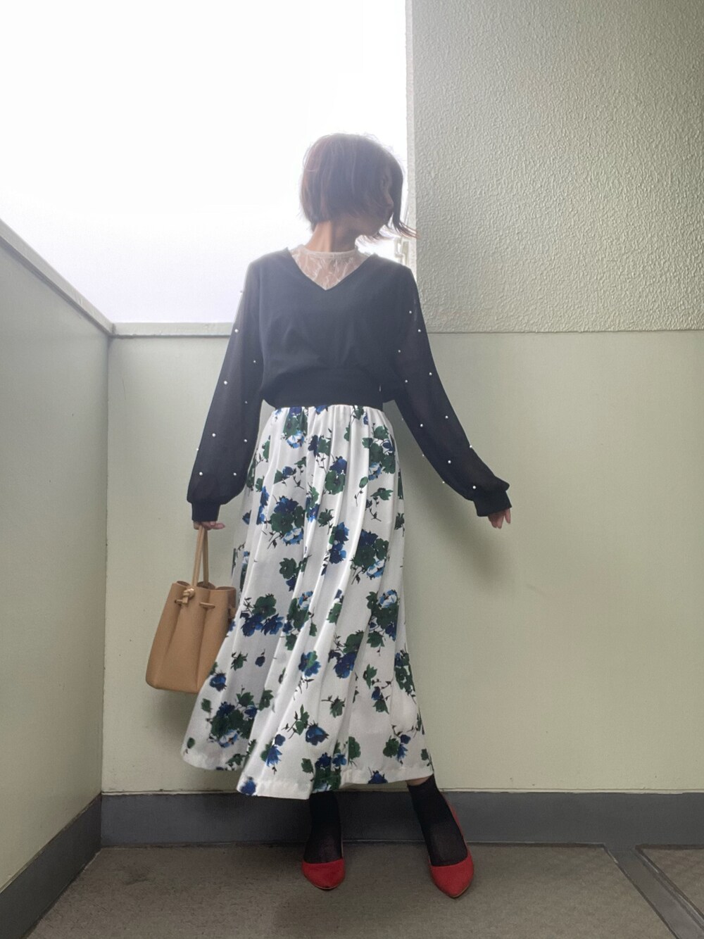 レッド系のパンプス、ホワイト系のスカート、ブラック系のバッグを着用したレディースの春コーディネートの1枚目の写真