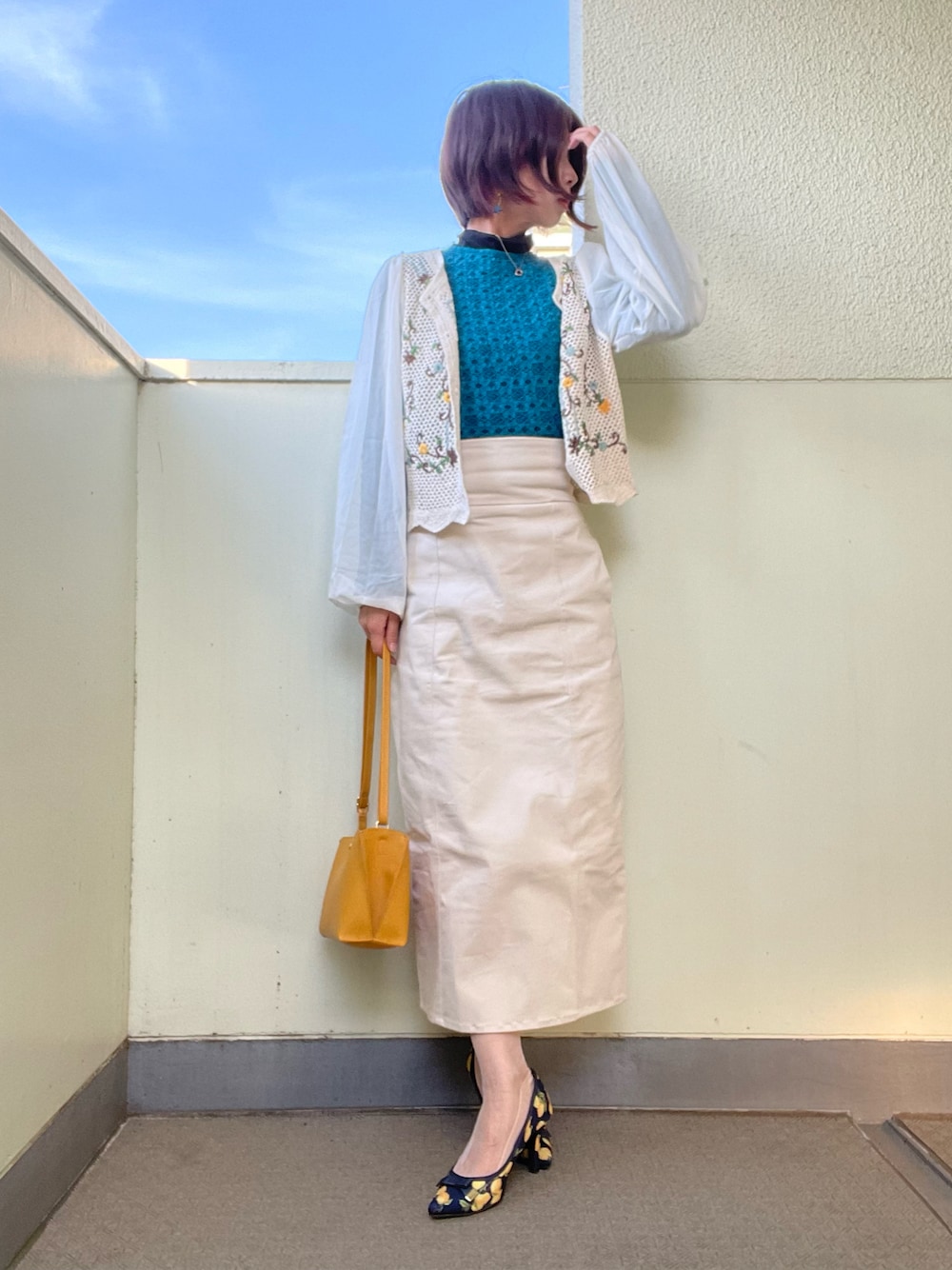 イエロー系のバッグ、ブルー系のシューズ、ブラック系のスカートを着用したレディースの春コーディネートの1枚目の写真