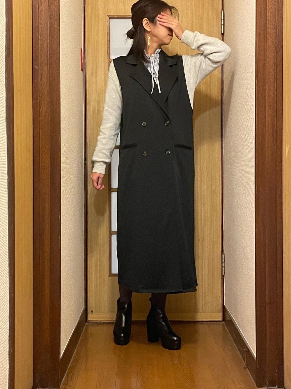 ブラック系のブーツ、ブラック系のベスト、ホワイト系のワンピースを着用したレディースの冬コーディネートの1枚目の写真