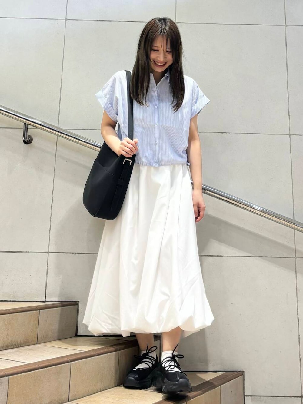 ブラック系のスニーカー、ホワイト系のスカート、ブラック系のショルダーバッグを着用したレディースの春コーディネートの1枚目の写真
