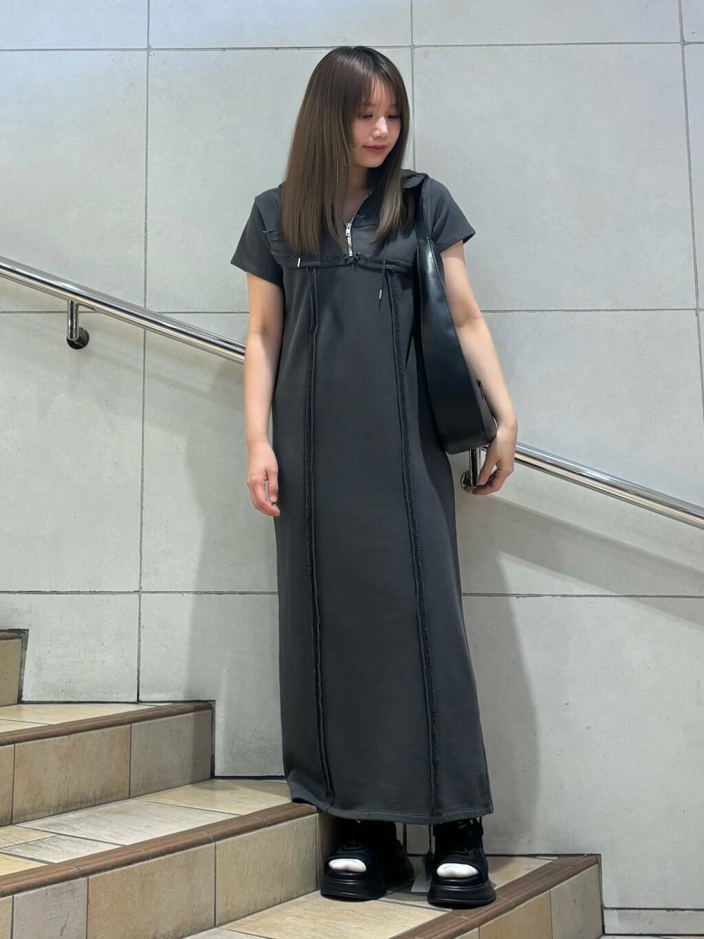 ブラック系のショルダーバッグ、ブラック系のサンダル、グレー系のワンピースを着用したレディースの春コーディネートの1枚目の写真