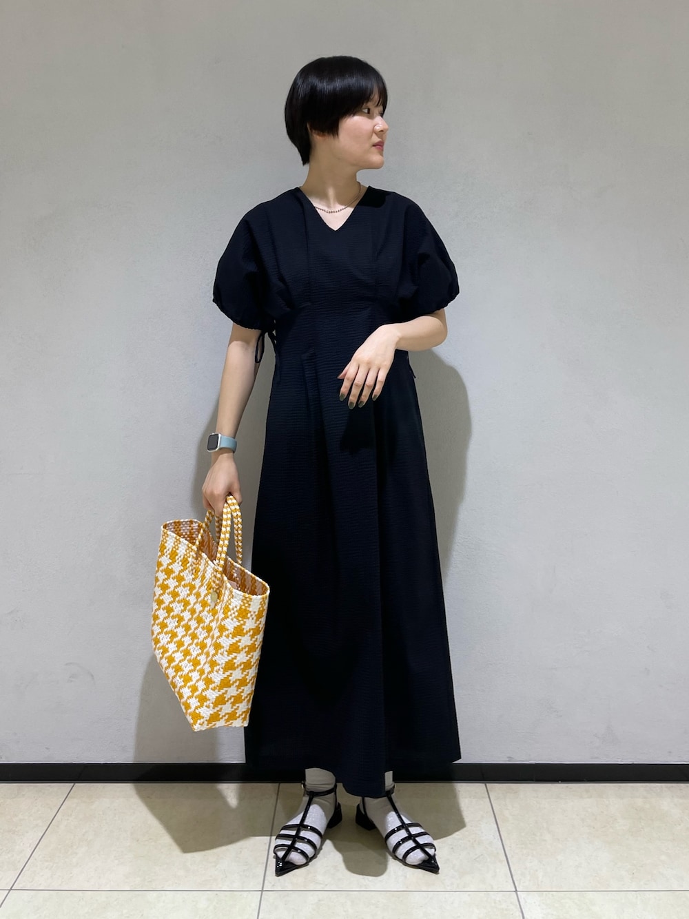 ブラック系のワンピース、イエロー系のトートバッグ、ブラック系のサンダルを着用したレディースの春コーディネートの1枚目の写真
