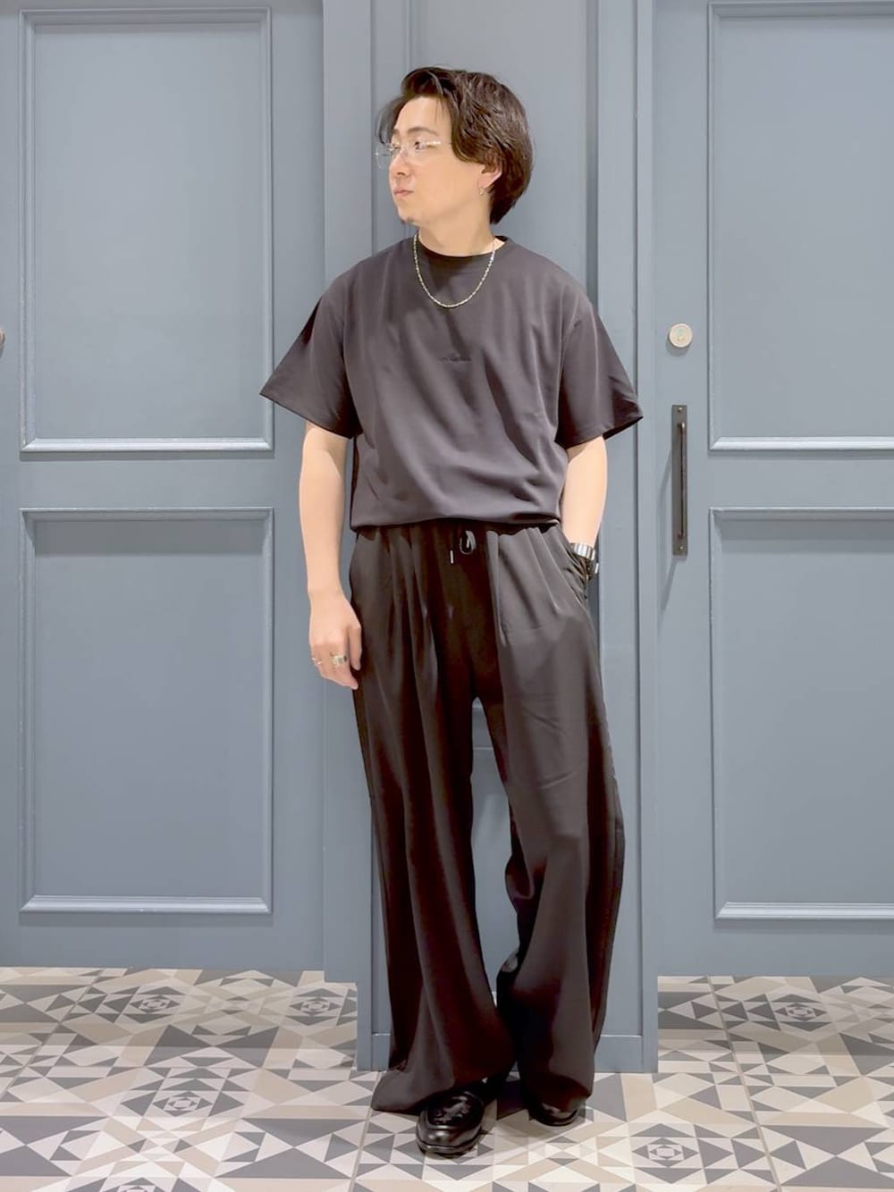 ブラック系のローファー、グレー系のスラックス、ブラック系のTシャツ/カットソーを着用したメンズの夏コーディネートの1枚目の写真