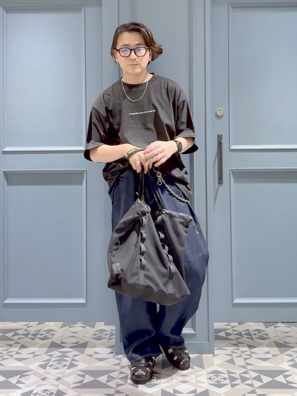 ブラック系のトートバッグ、ブラック系のサンダル、ブルー系のデニムパンツを着用したメンズの夏コーディネートの1枚目の写真