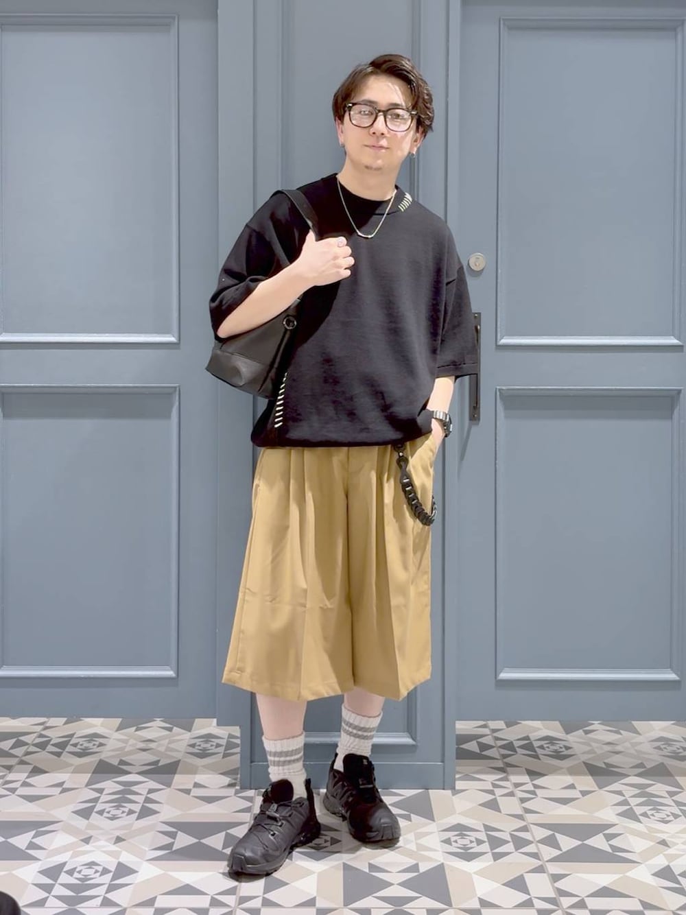 ブラック系のスニーカー、ブラック系のハンドバッグ、ベージュ系のスラックスを着用したメンズの春コーディネートの1枚目の写真