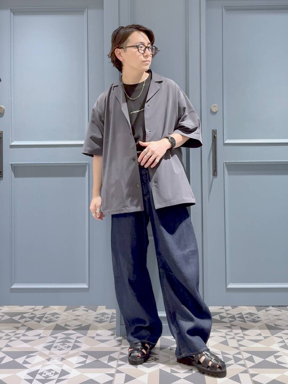 グレー系のシャツ/ブラウス、ブラック系のサンダル、ブルー系のデニムパンツを着用したメンズの夏コーディネートの1枚目の写真