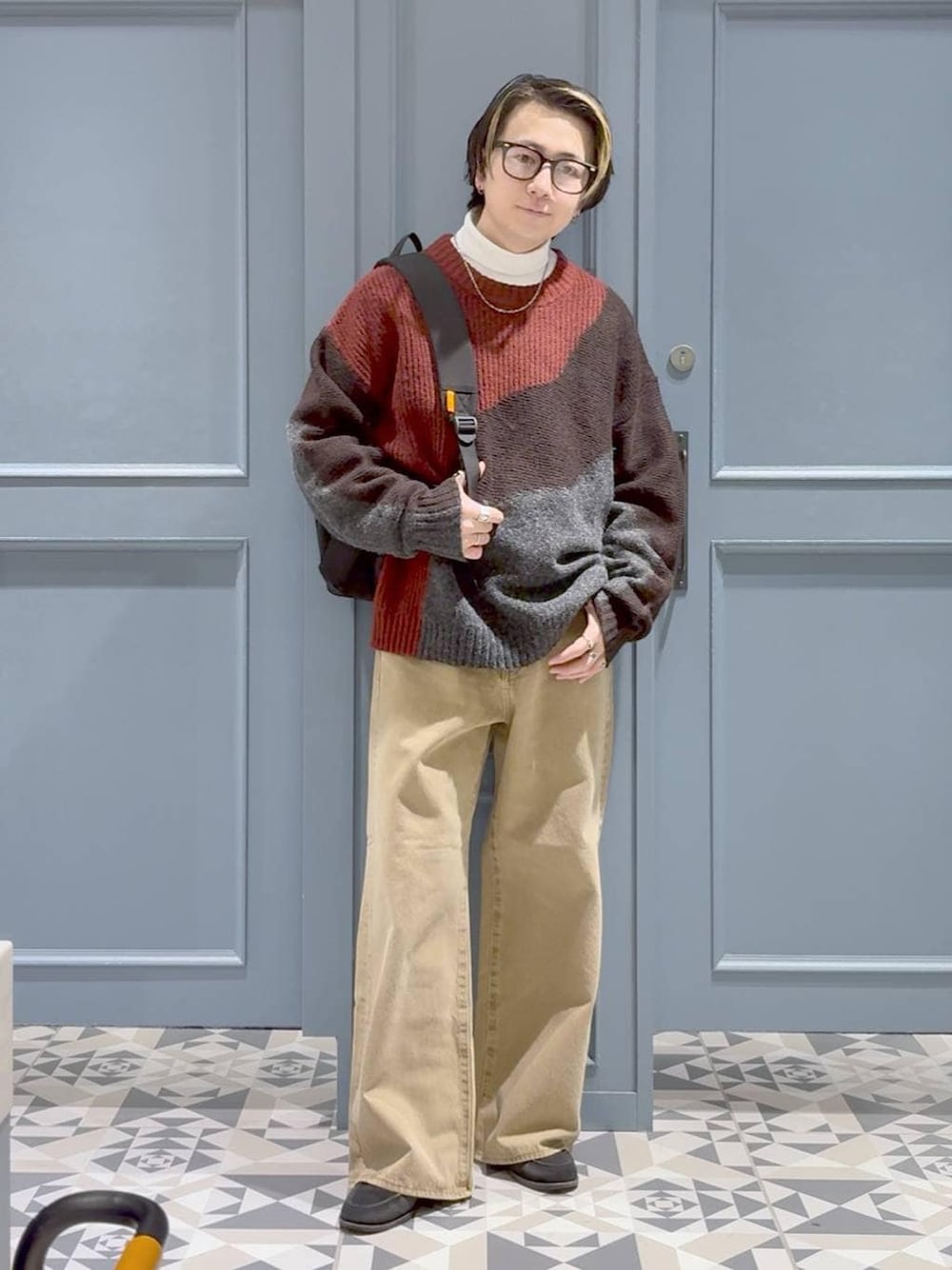 ベージュ系のデニムパンツ、ブラック系のバックパック/リュック、レッド系のニット/セーターを着用したメンズの冬コーディネートの1枚目の写真