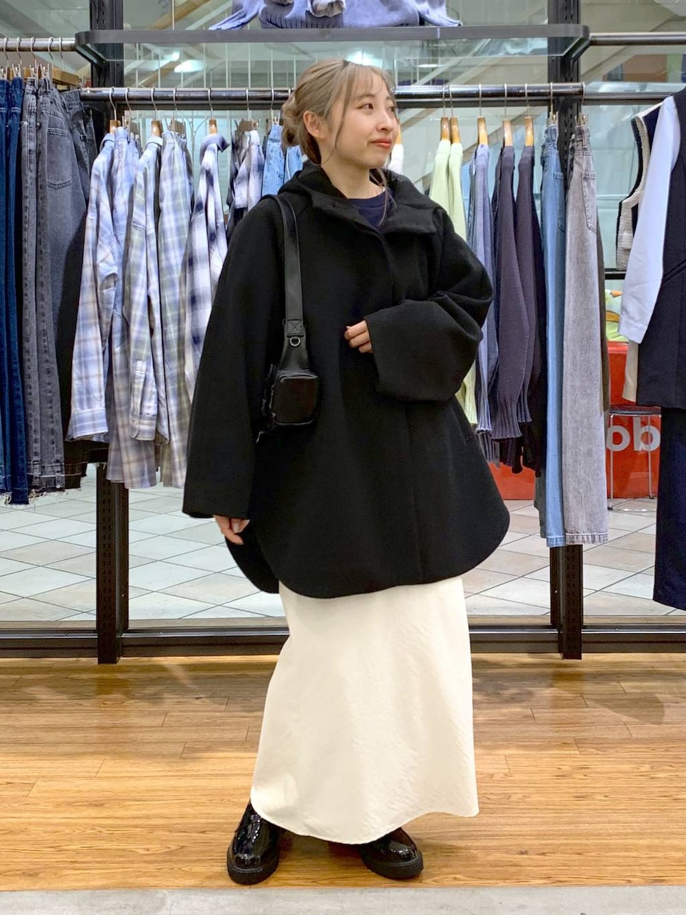 ブラック系のポンチョ、ホワイト系のスカート、ブラック系のショルダーバッグを着用したレディースの冬コーディネートの1枚目の写真