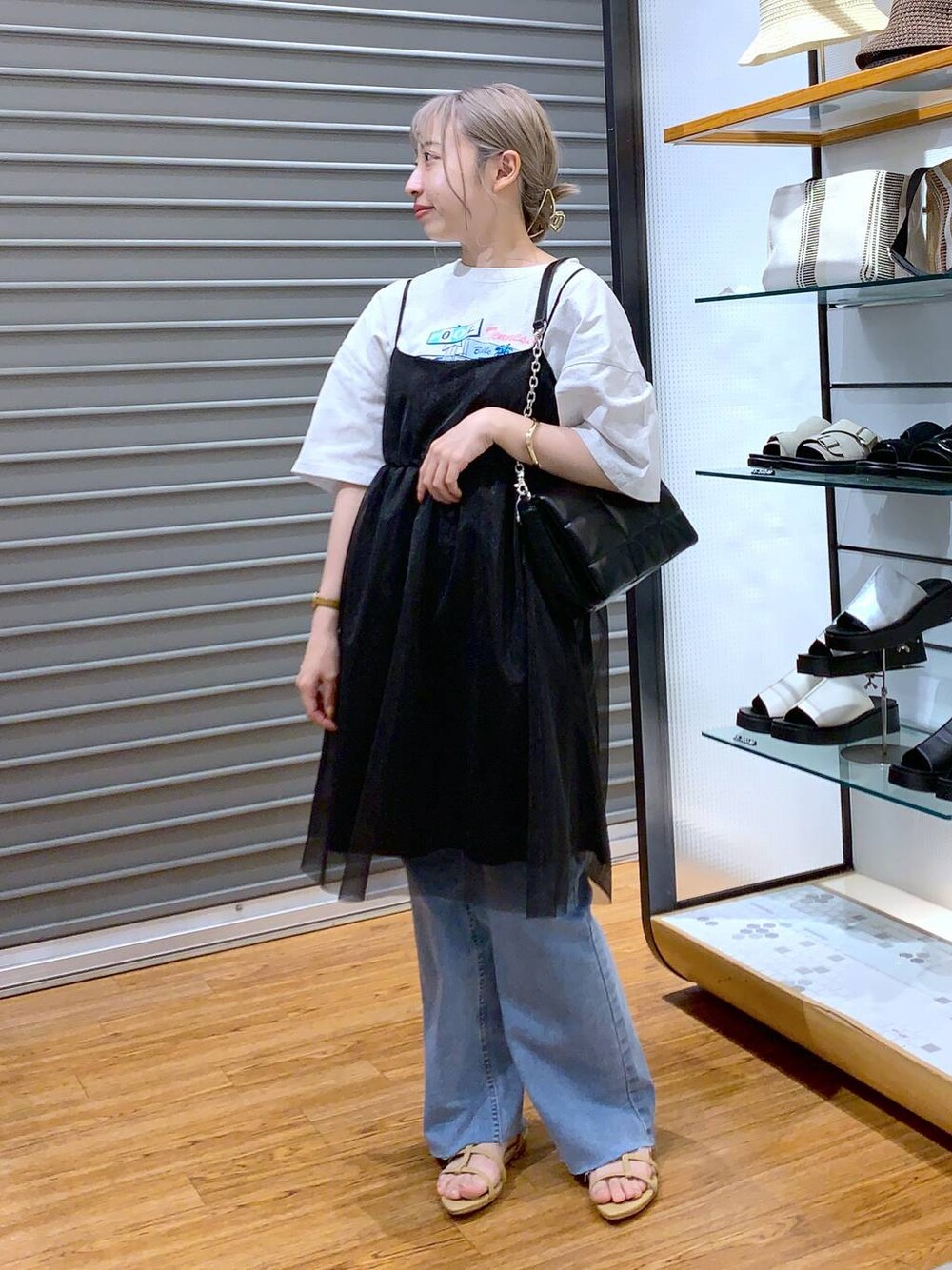 ブラック系のショルダーバッグ、ベージュ系のサンダル、ブルー系のデニムパンツを着用したレディースの夏コーディネートの1枚目の写真