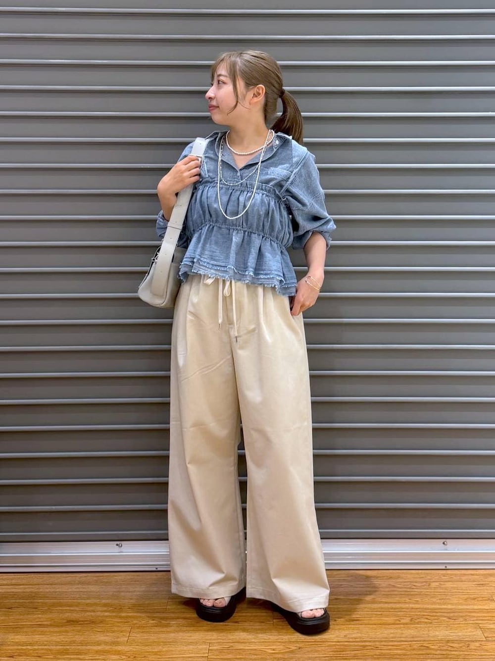 グレー系のショルダーバッグ、ホワイト系のサンダル、ブルー系のシャツ/ブラウスを着用したレディースの夏コーディネートの1枚目の写真