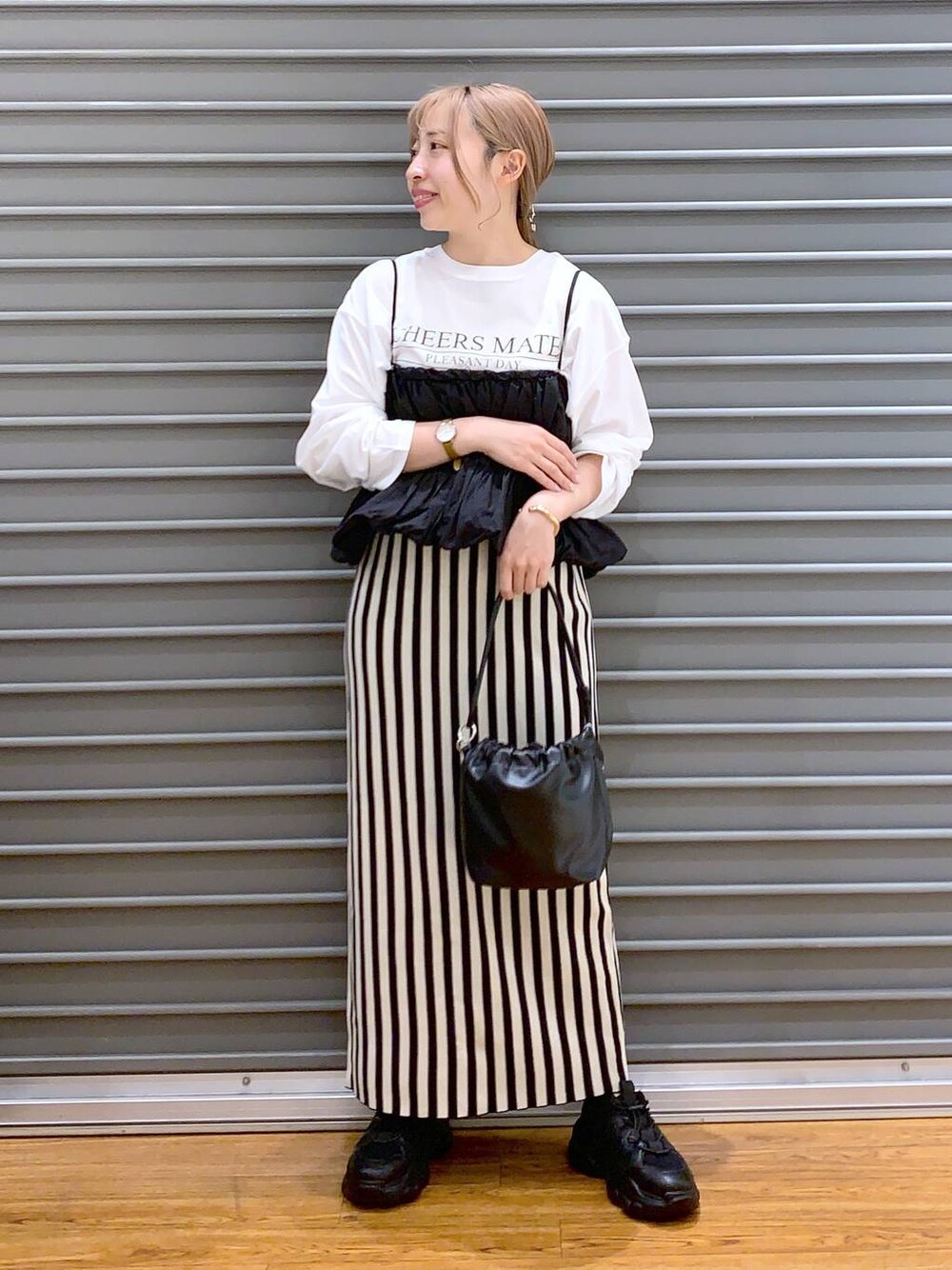 ブラック系のショルダーバッグ、ブラック系のスニーカー、ホワイト系のスカートを着用したレディースの春コーディネートの1枚目の写真