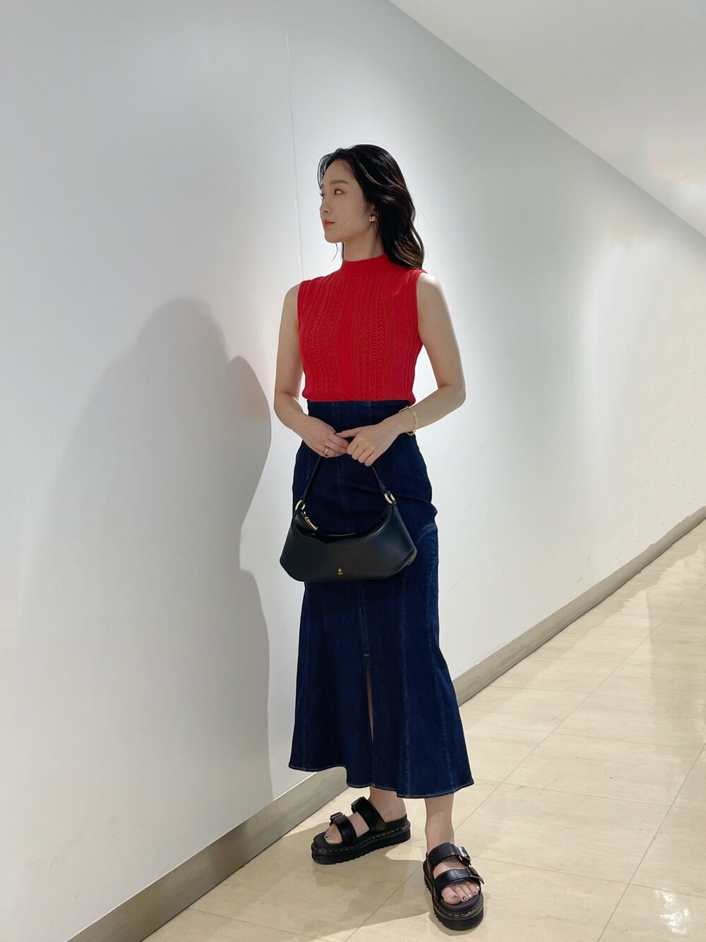 ブラック系のハンドバッグ、レッド系のニット/セーター、ブルー系のデニムスカートを着用したレディースの夏コーディネートの1枚目の写真