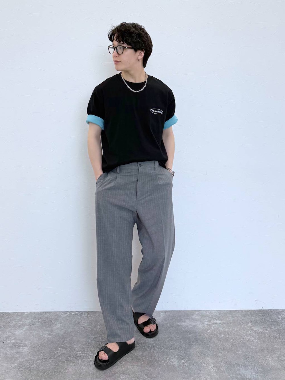 グレー系のスラックス、ブルー系のTシャツ/カットソー、ブラック系のサンダルを着用したメンズの夏コーディネートの1枚目の写真