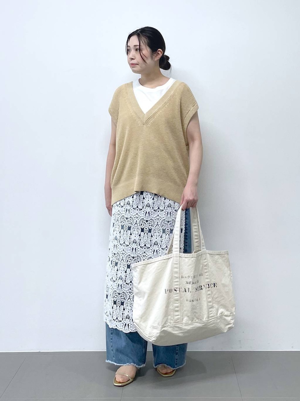 ブルー系のデニムパンツ、ホワイト系のタンクトップ、ベージュ系のベストを着用したレディースの春コーディネートの1枚目の写真